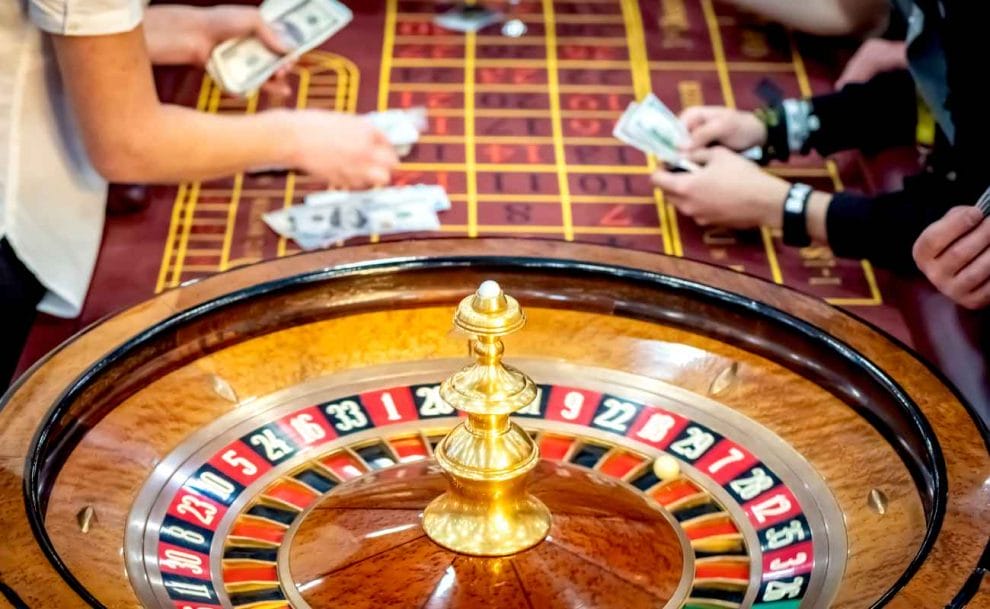 A roulette wheel with people counting money in the background. 