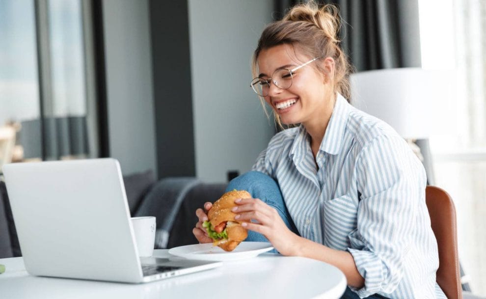  A woman eating a burger in front of her laptop.