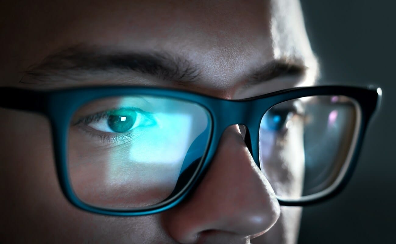 A close-up of a man wearing glasses looking at a digital screen.
