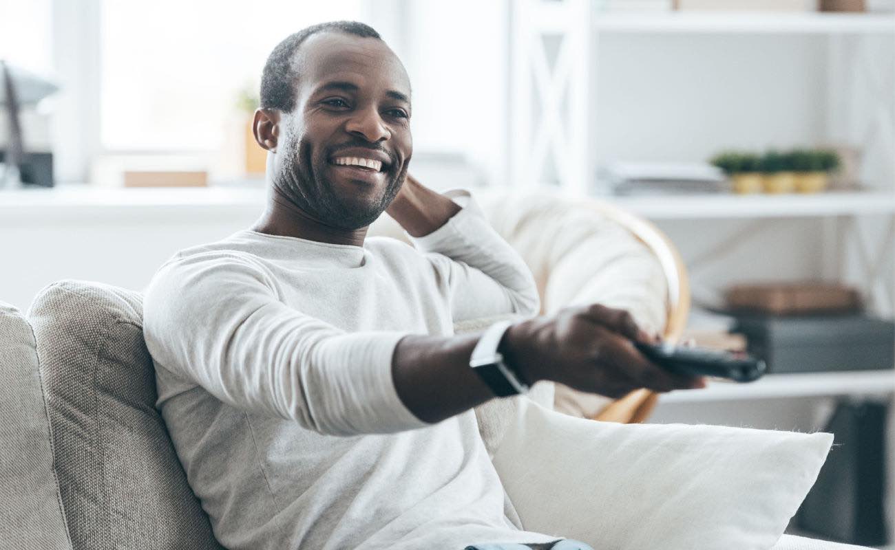 A man holding a TV remote while watching from his couch.