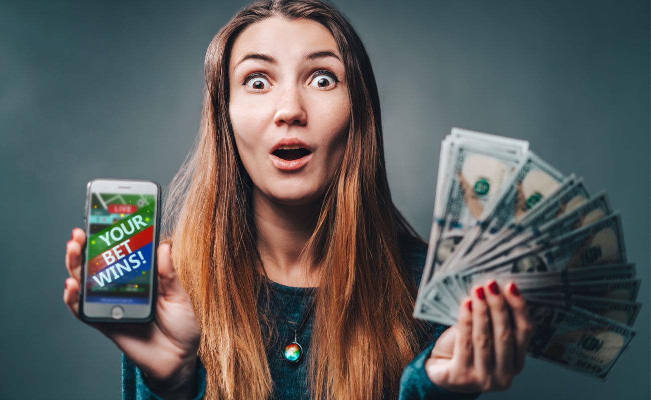 A woman holding a handful of money and a smartphone screen that says, “Your bet wins!”