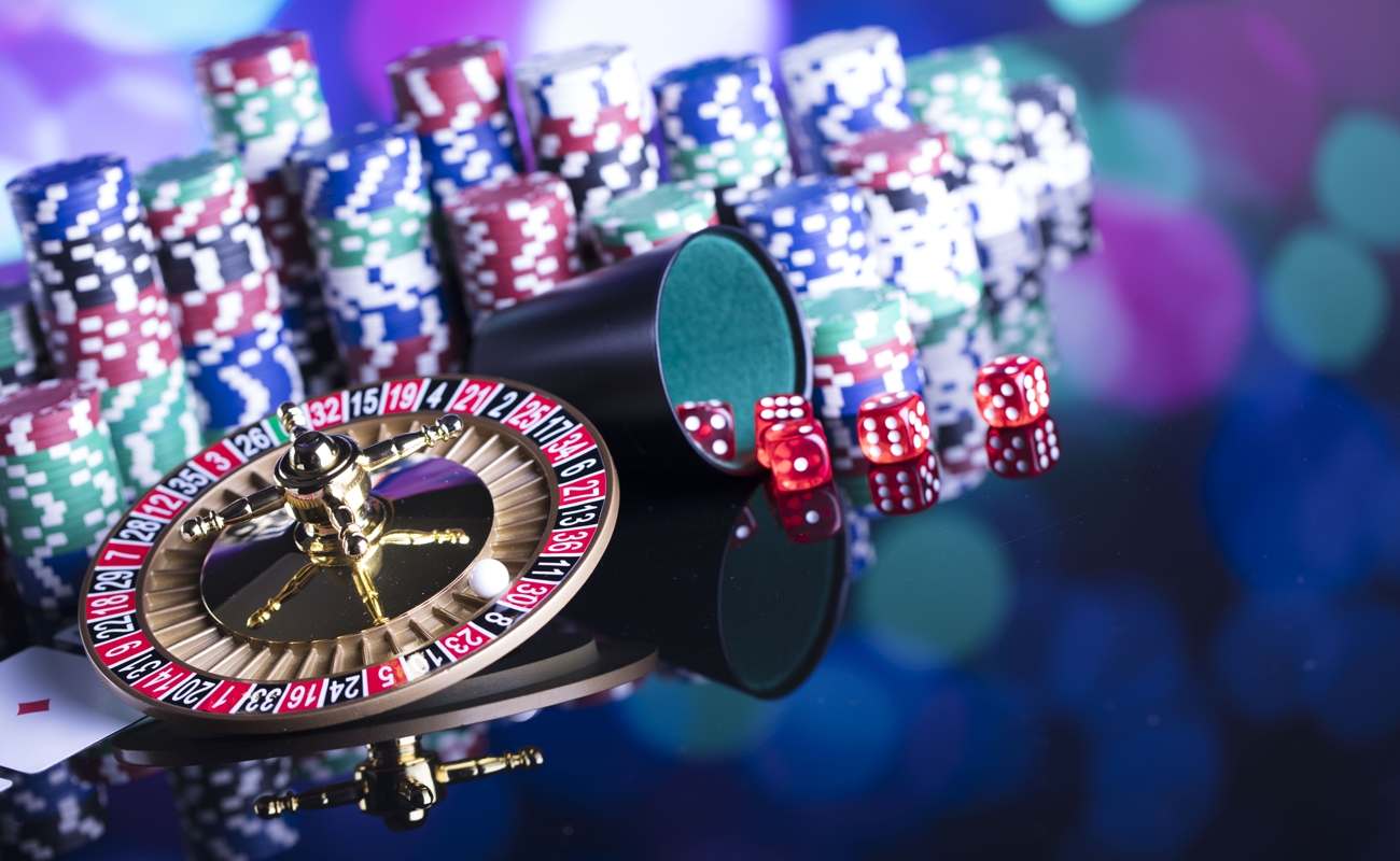 A variety of casino games, including a mini-roulette wheel, craps dice and playing cards in front of stacks of casino chips.