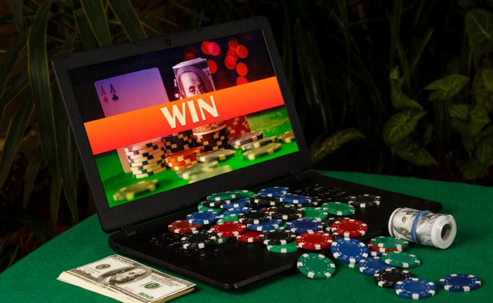 Poker chips and money on a laptop displaying “WIN” on its screen..