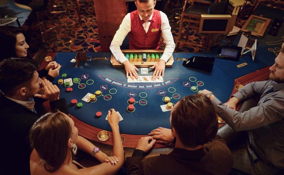 A group of players sitting around a poker table with the croupier in the middle.