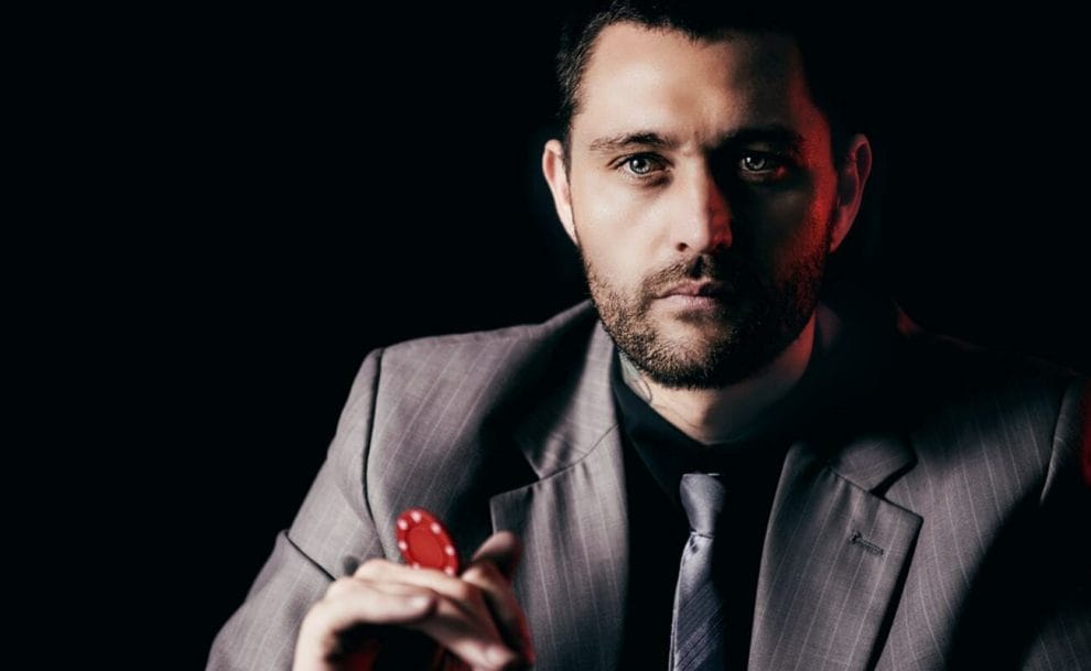 A man in a suit with a red poker chip in his hand.