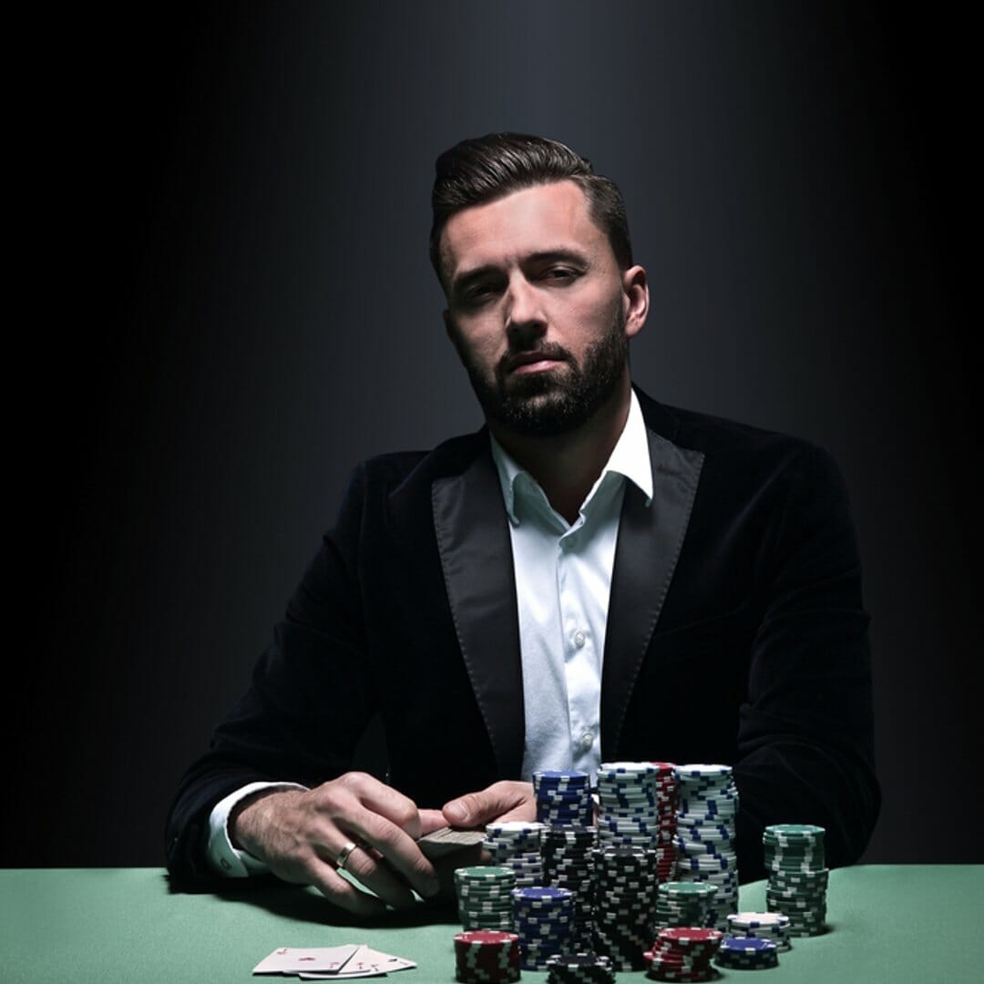 A man in a suit sitting at a poker table with chips and cards.
