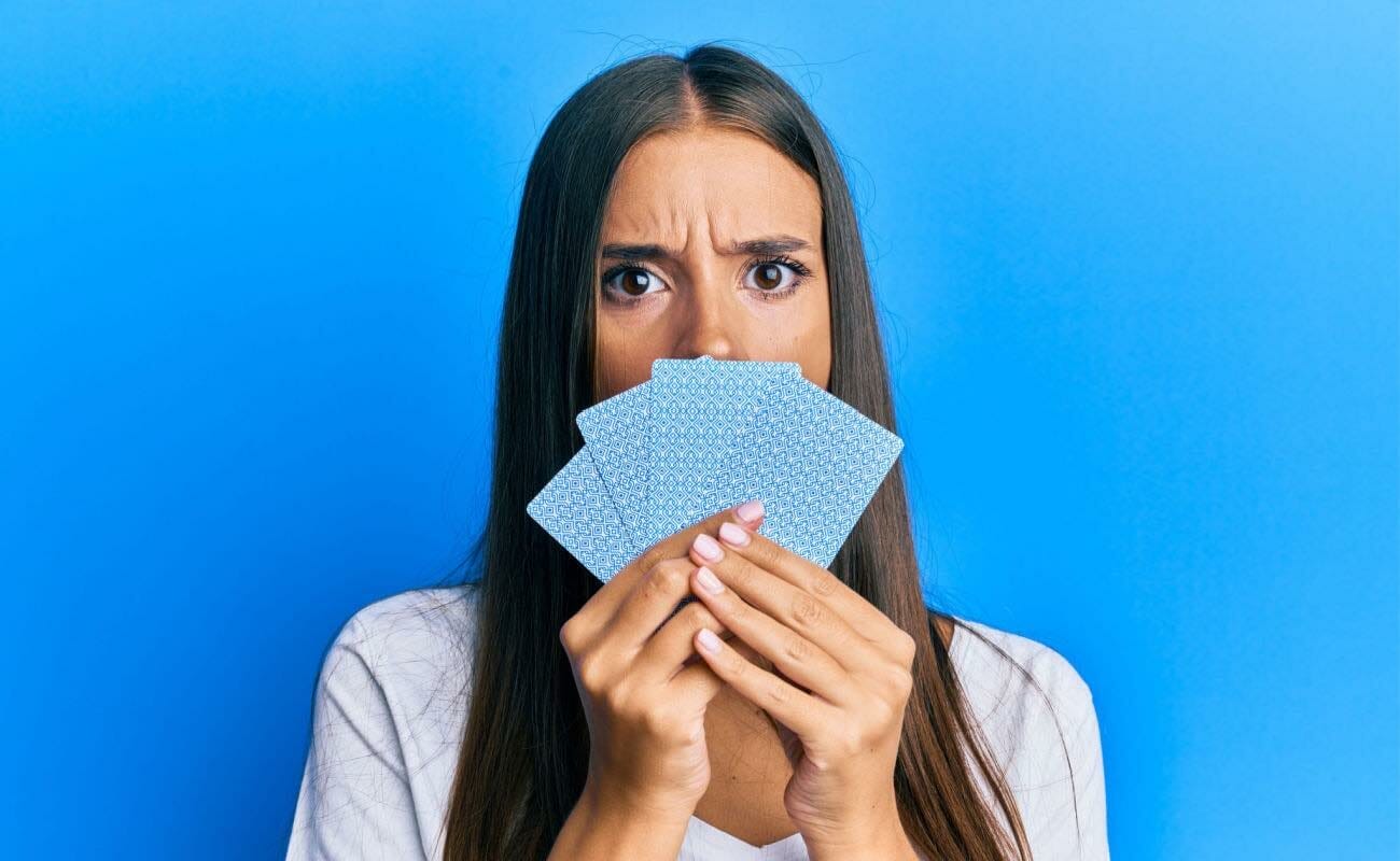 woman holding playing cards up to her face with a shocked expression.