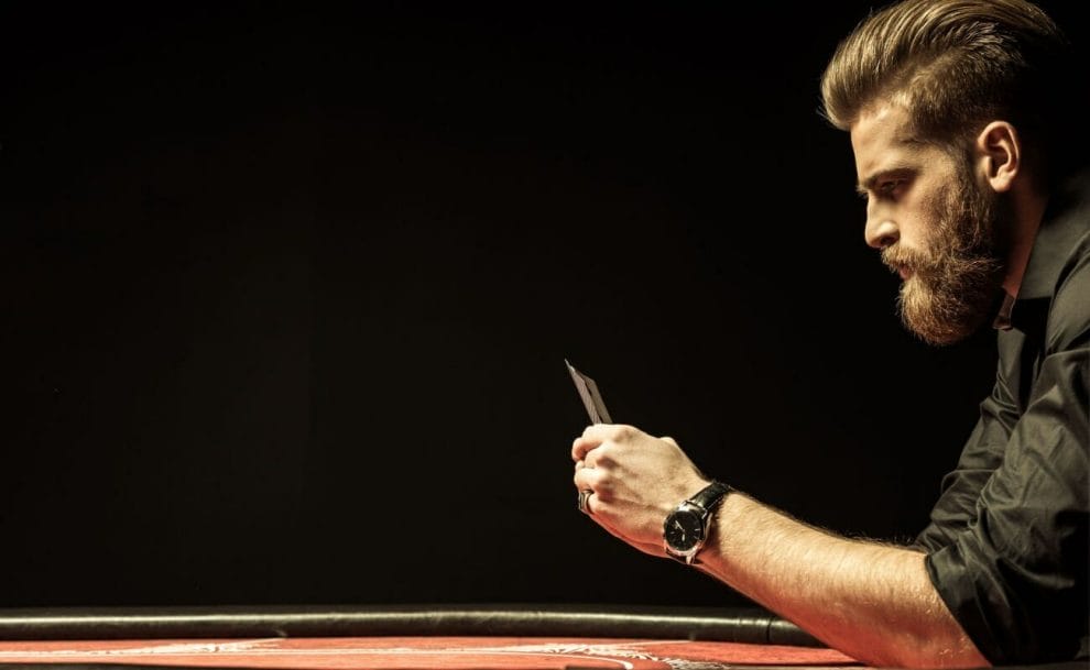 A bearded man focusing intensely on playing cards at a casino table.