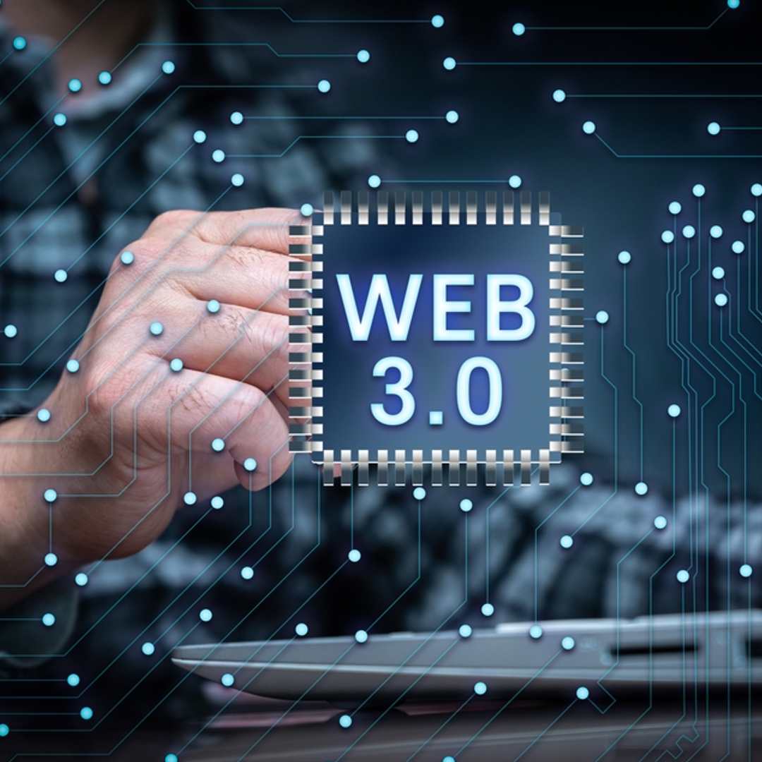 Web 3.0 written on a data chip with a person on a laptop behind it.