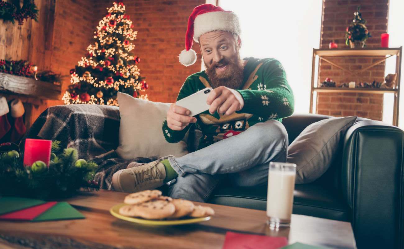 A man wearing a Christmas sweater playing on his smartphone.