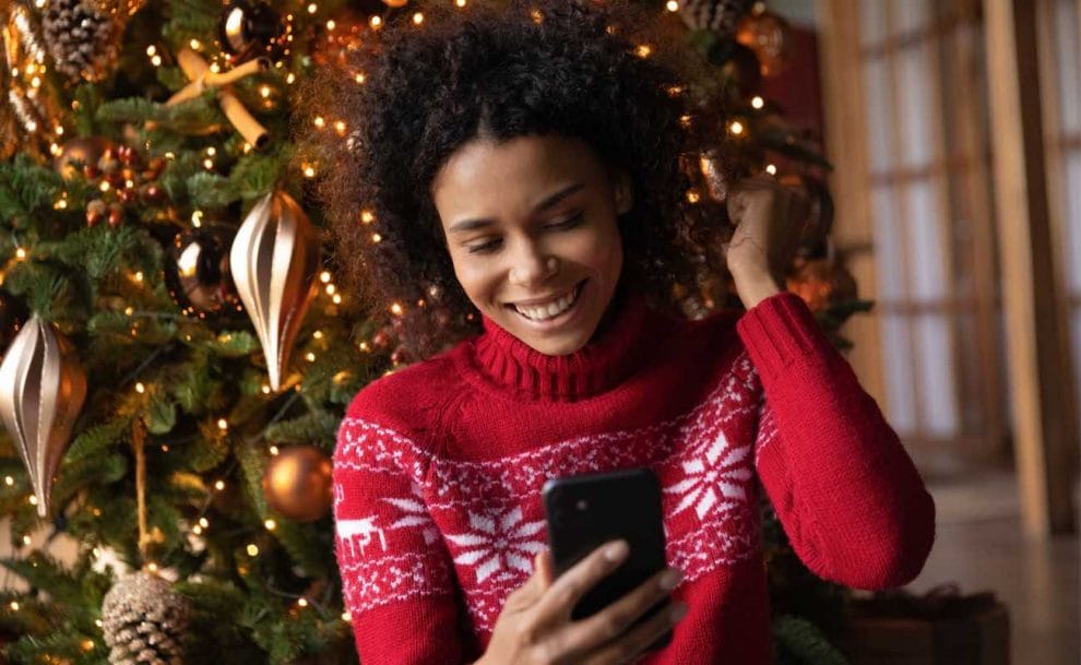 A smiling woman wearing a Christmas sweater looking at her smartphone.
