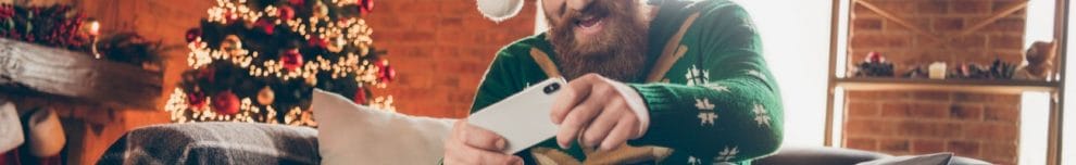 A man wearing a Christmas sweater playing on his smartphone.