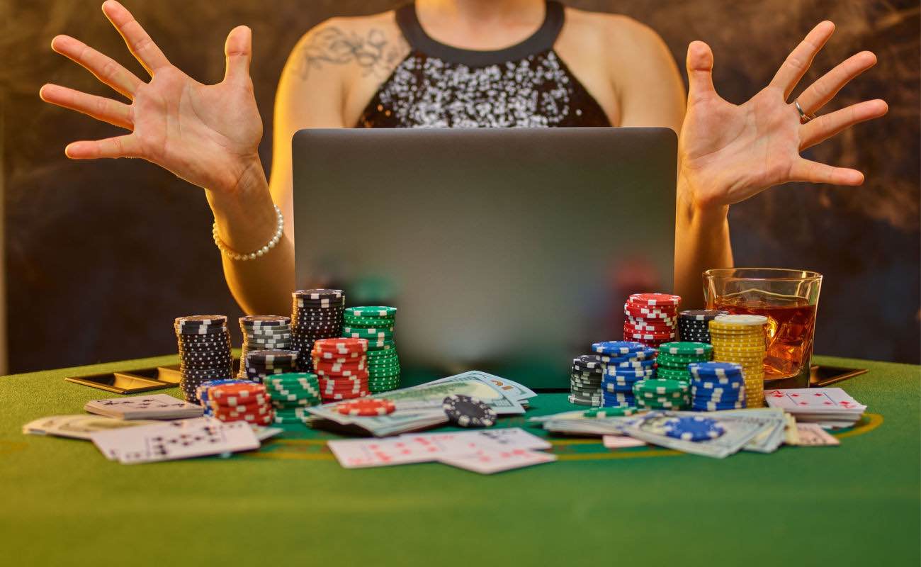 A laptop, casino chips and cards on a green felt table.