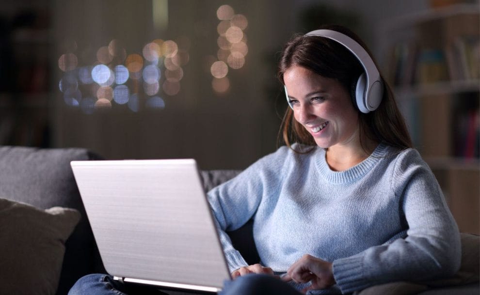 A smiling woman wearing headphones looking at a laptop.