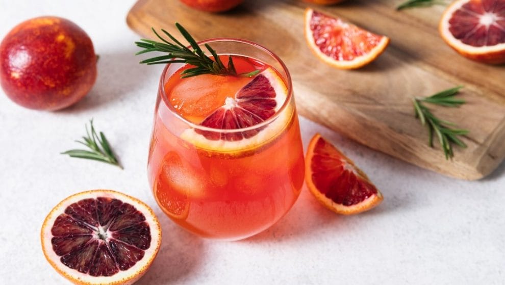 A blood orange soda on a table next to a cutting board with slices of blood oranges.