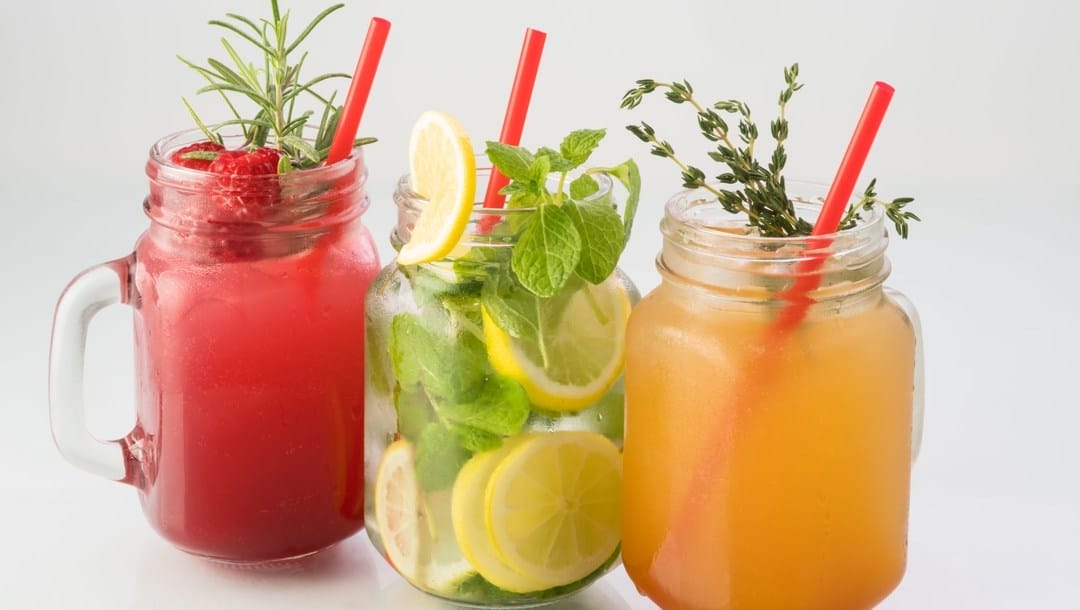 Three non-alcoholic drinks in jars with straws.