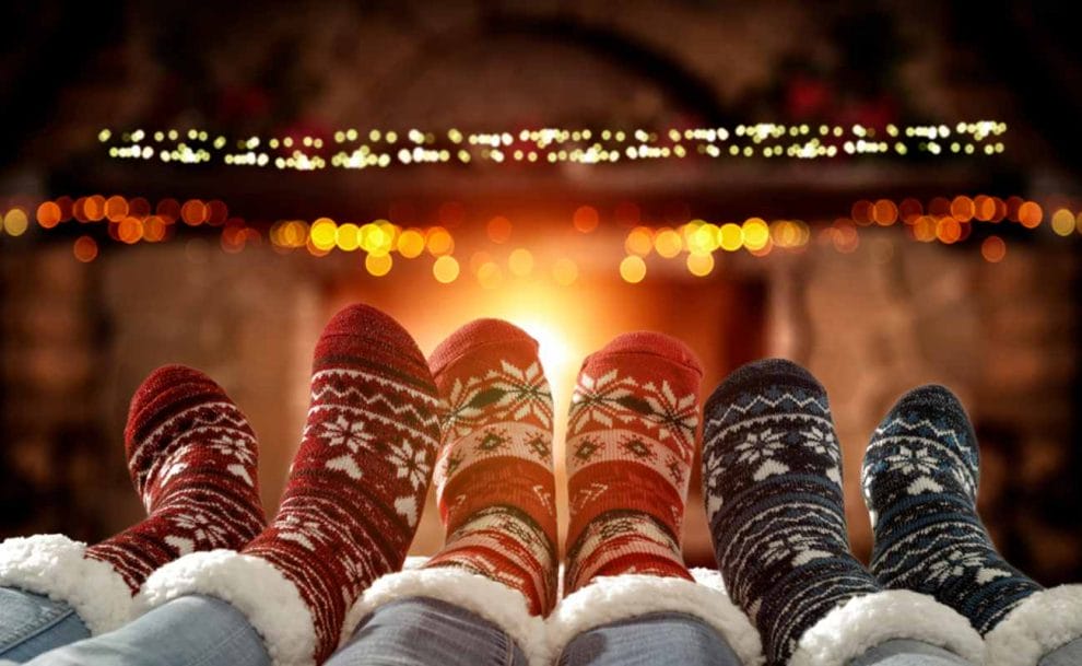 A family sitting in front of the fire with Christmas socks on. 