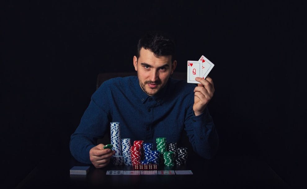 Poker player seated at a poker table with playing cards in his hand and stacks of poker chips in front of him.
