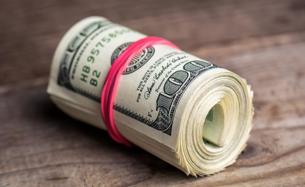 A roll of dollars bound with a pink rubber band on a wooden table.