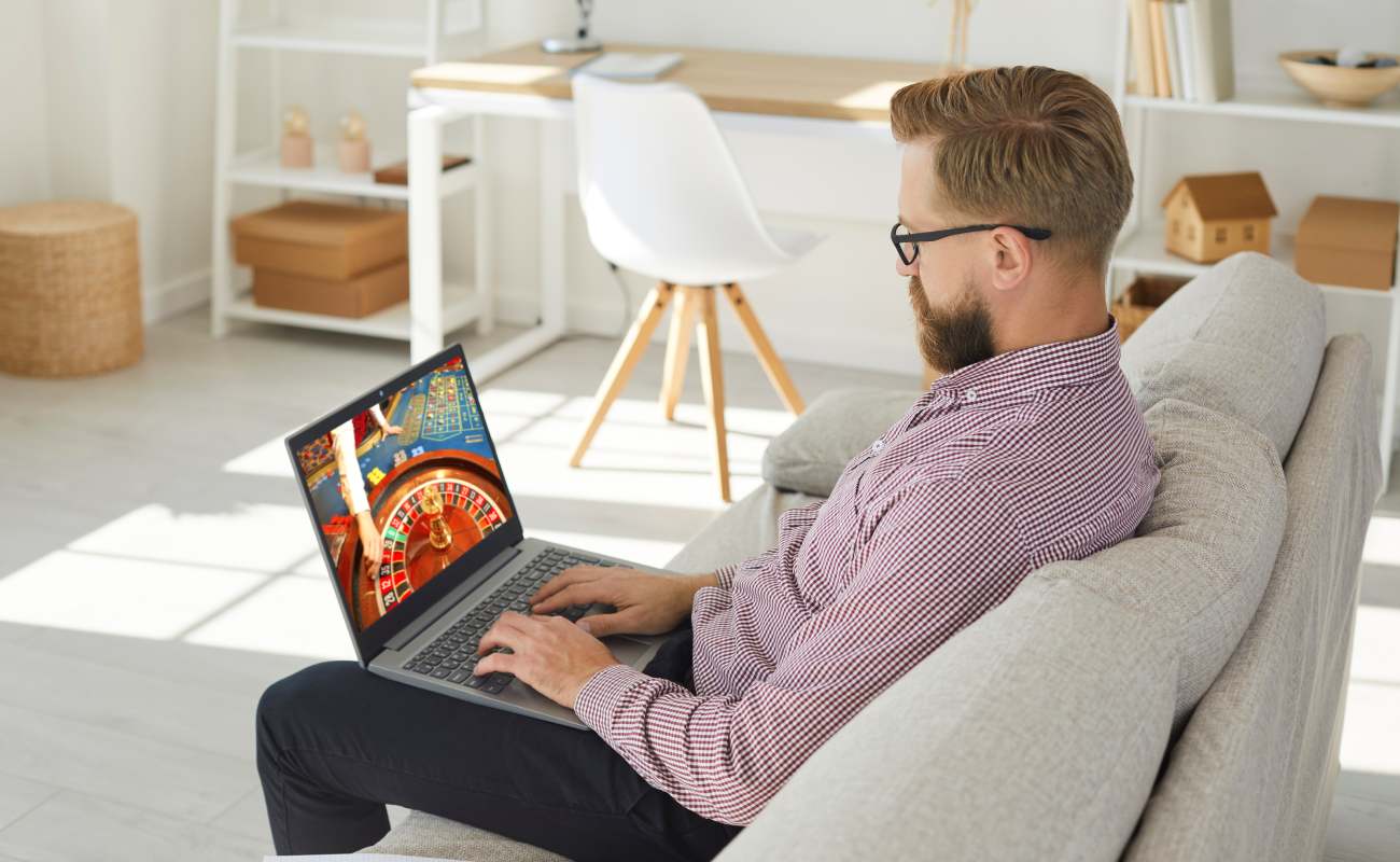 A man sitting on a couch playing online casino games on a laptop.