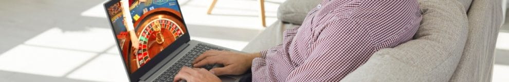 A man sitting on a couch playing online casino games on a laptop.