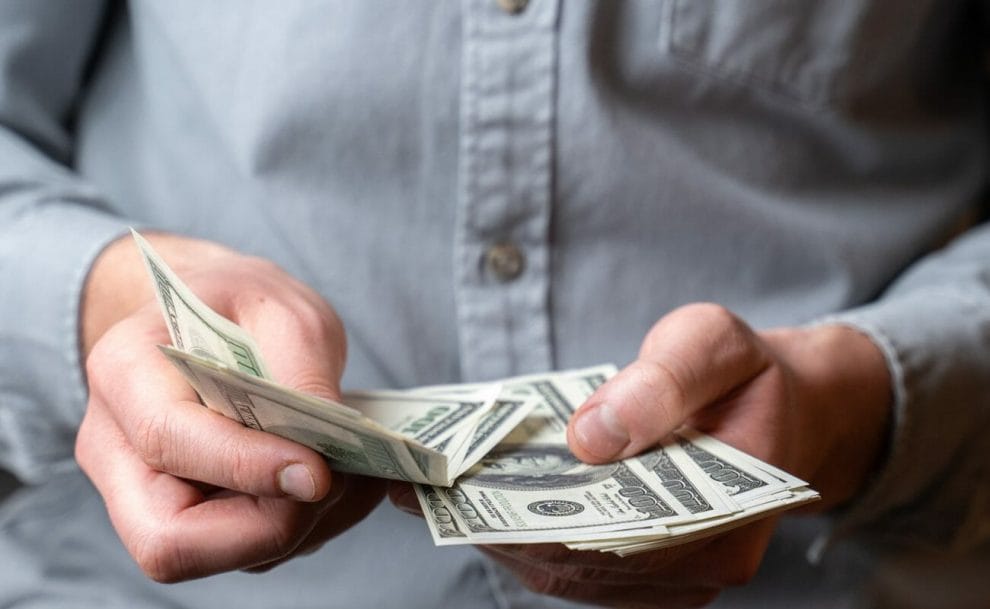 A man in a blue shirt counting down $100 bills.