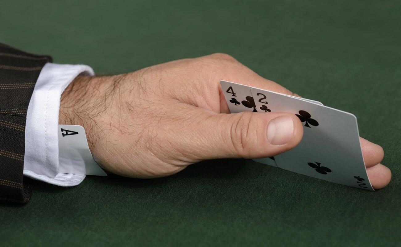  A poker player with an ace up his sleeve looks at his hole cards: a four and two of clubs.