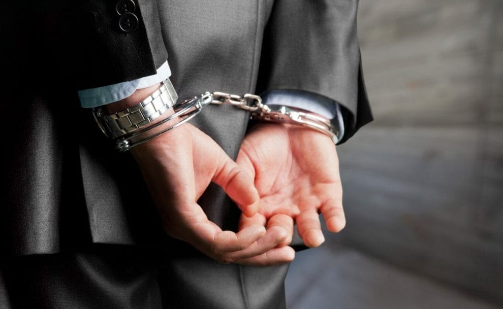 A suited person’s hands cuffed behind their back.