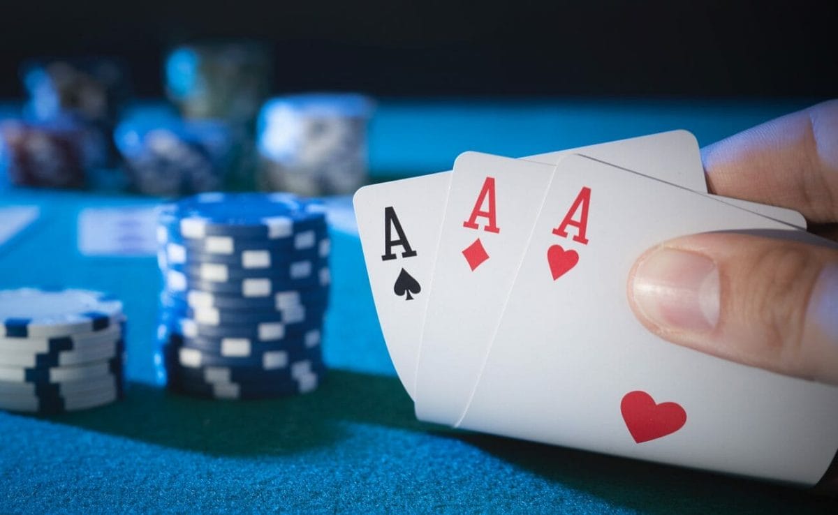 A player reveals three aces next to two stacks of poker chips.