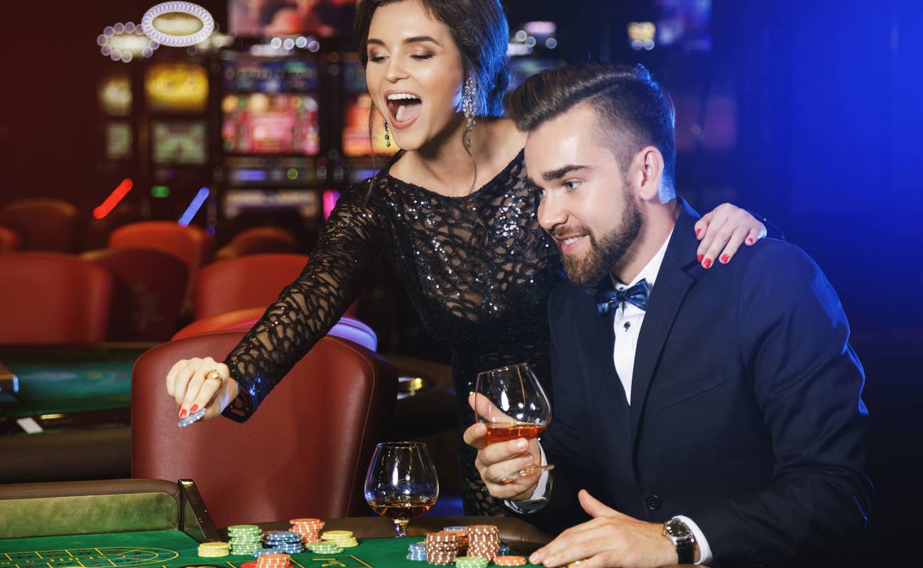A well-dressed couple with drinks at a gambling table in a casino.
