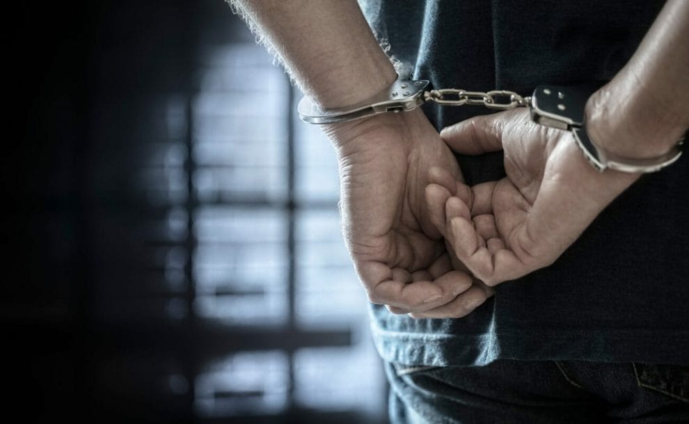 A man in handcuffs with his hands behind his back in a prisoner’s uniform.