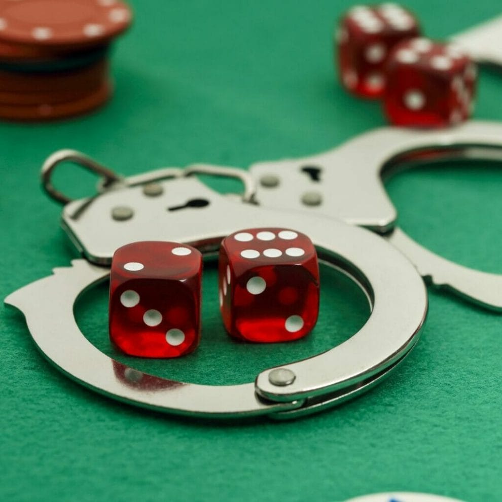 A pair of dice sitting inside a pair of handcuffs on a gambling table.