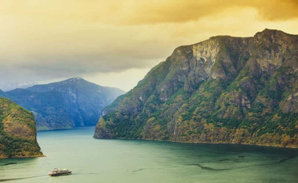 A cruise ship sailing through a fjord at sunset.