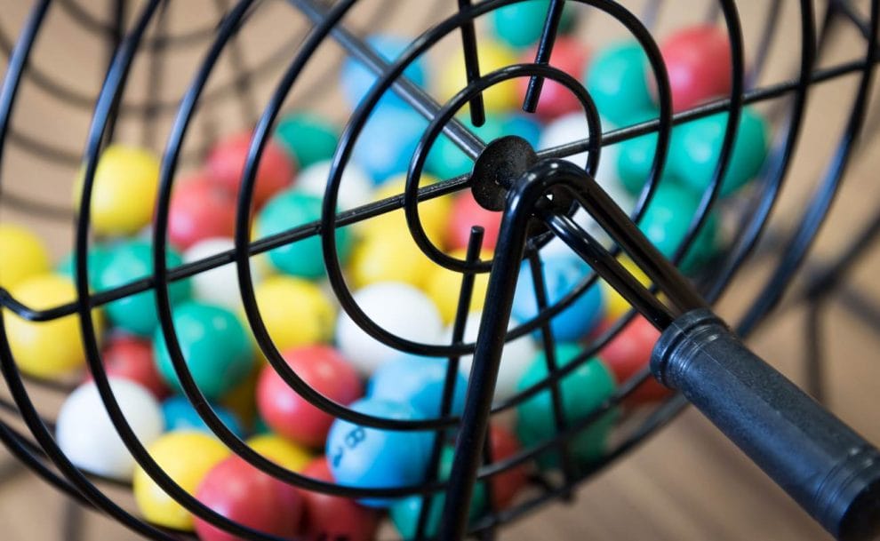 A black bingo cage with red, yellow, blue, green and white balls inside.