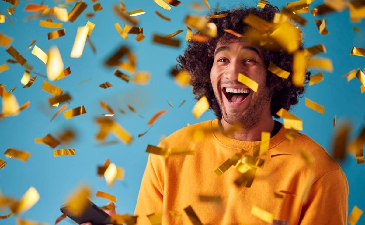 A laughing man in a yellow sweater surrounded by falling yellow ticker tape.