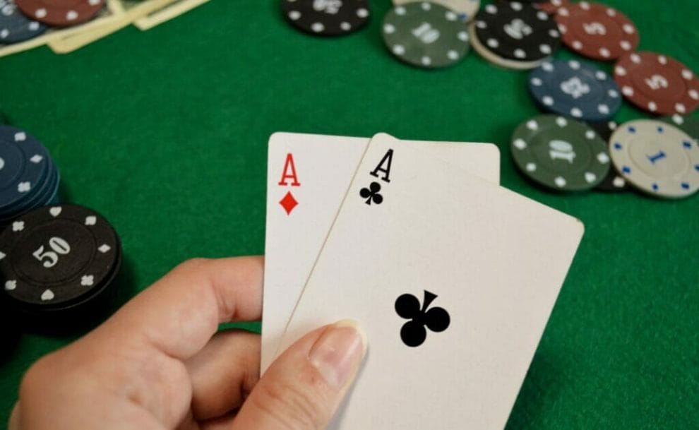 A poker player reveals two aces with poker chips on the table in the background.