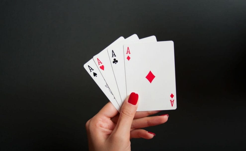 A person holding up four aces against a black background.