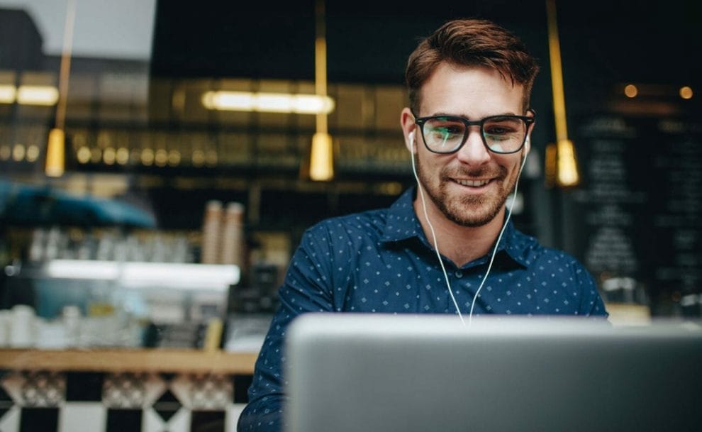 A man wearing earphones sitting in a cafe looking at his laptop.