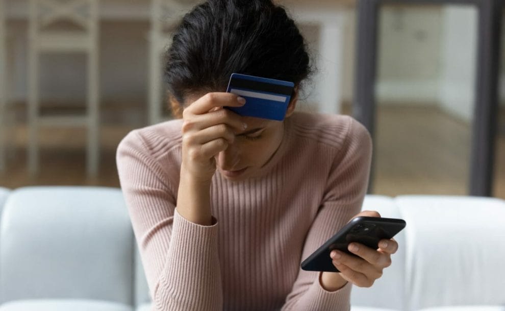 A woman holding her credit card to her head with her phone in the other hand