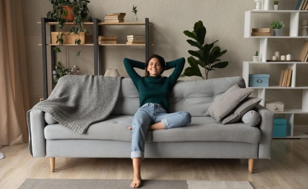 A woman relaxing on a gray couch with her hands behind her head