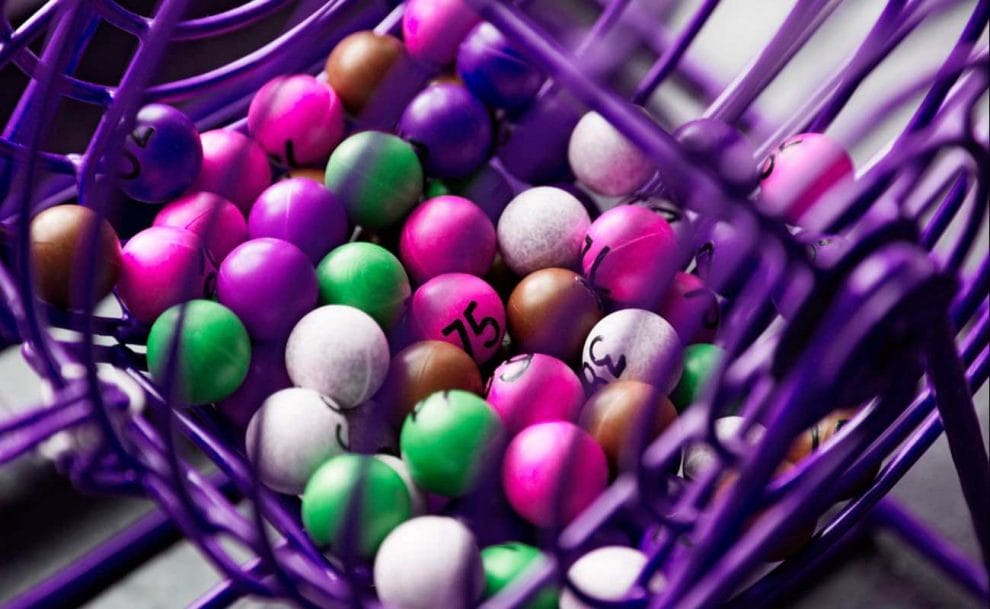  Green, white, brown and magenta bingo balls in a purple bingo cage.