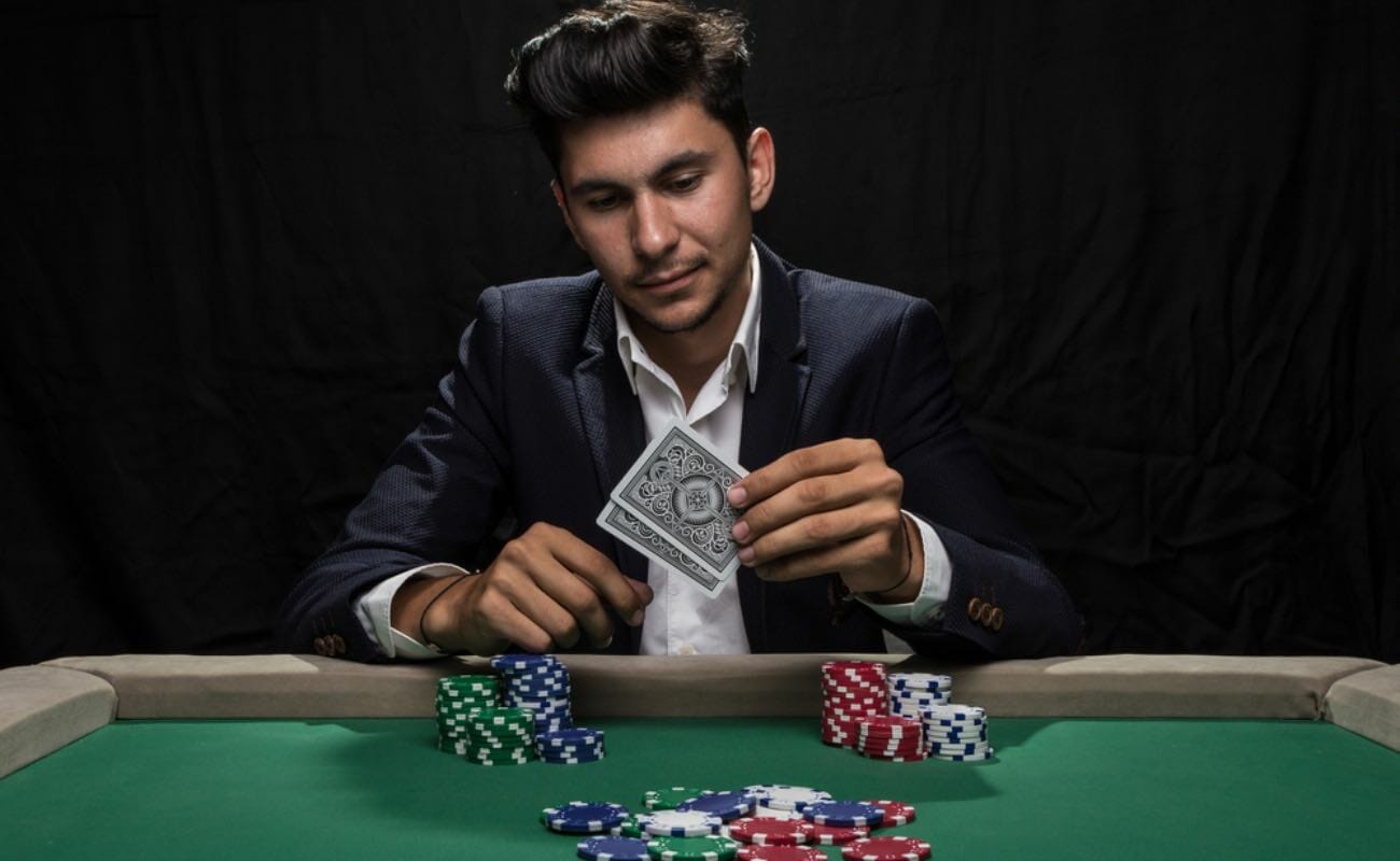 A man holding two cards at a poker table strewn with chips.