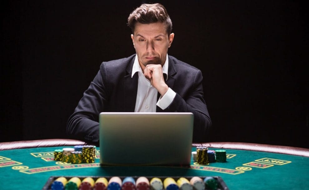  A person concentrates while using their laptop on a casino table. There are stacks of poker chips on either side of the laptop.