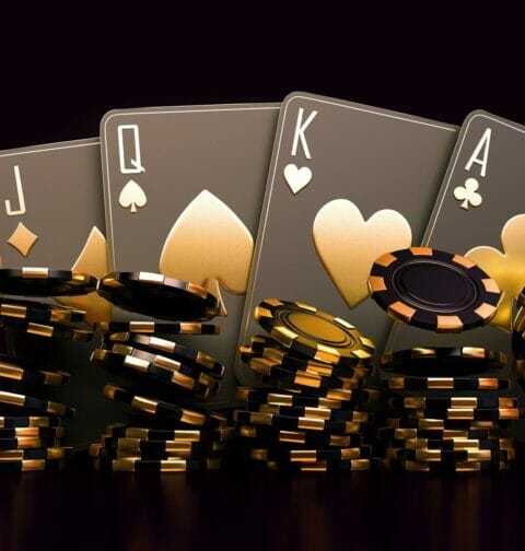 Four black and gold playing cards sit behind stacks of black and gold poker chips.