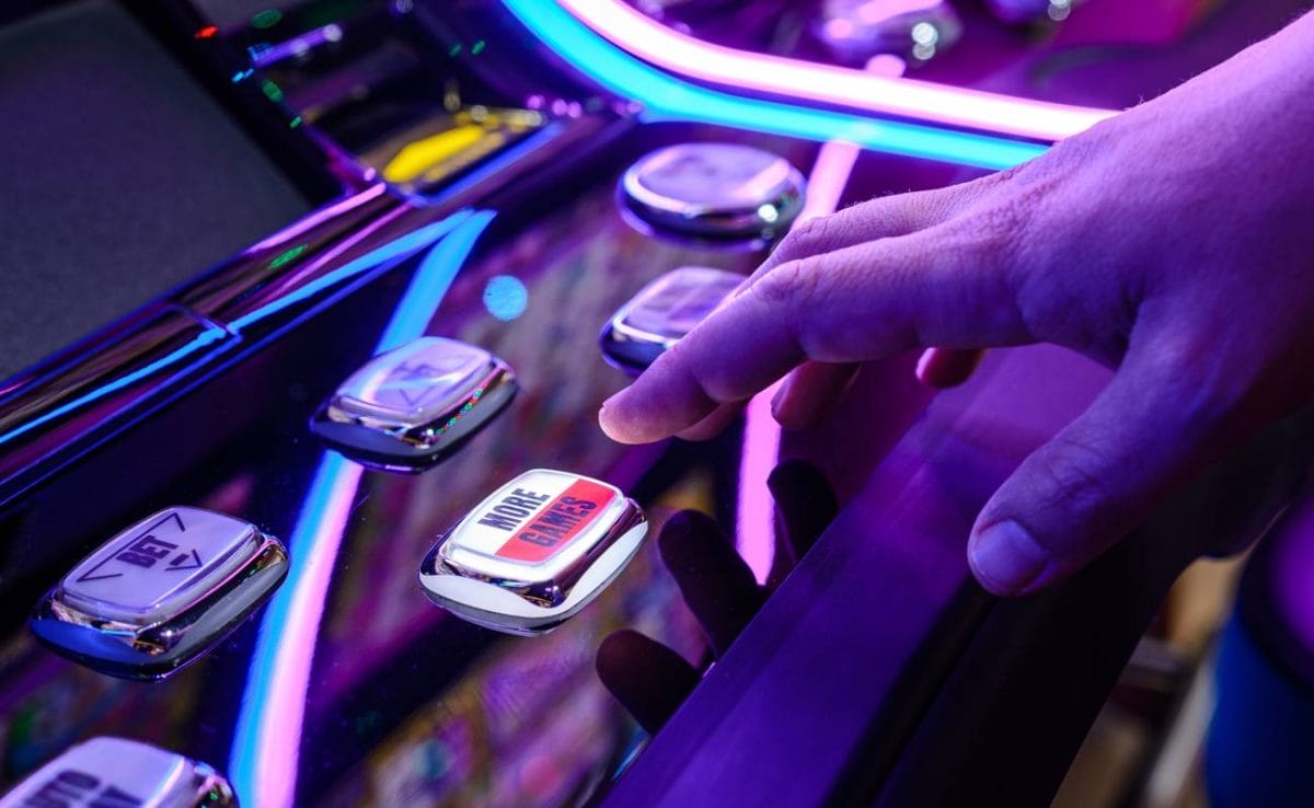 A person’s hand reaches to press the More Games button on a slot machine.