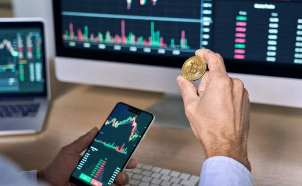A businessman holding a gold bitcoin between two fingers.