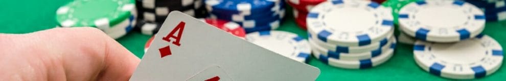 A hand holding an ace playing card with poker chips on a green table.