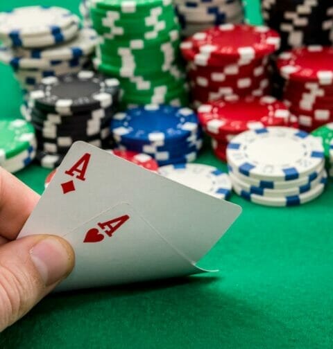 A hand holding an ace playing card with poker chips on a green table.