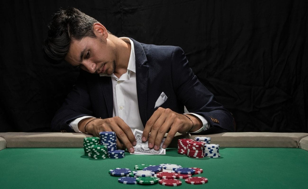 A poker player wearing a suit checks their cards before placing a bet.