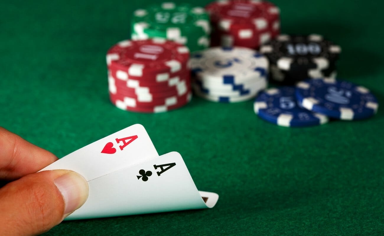 A poker player checks their hole cards and sees two aces. Their poker chips are on the table behind their cards.